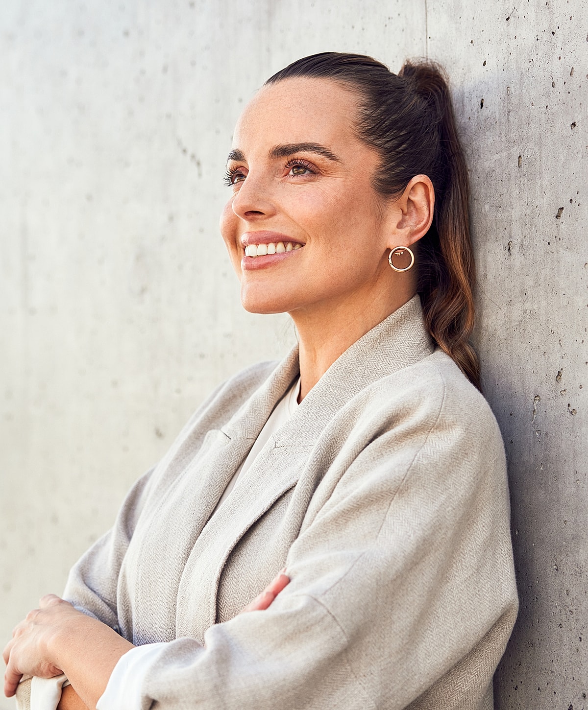 Smiling woman in stylish outfit against concrete wall.